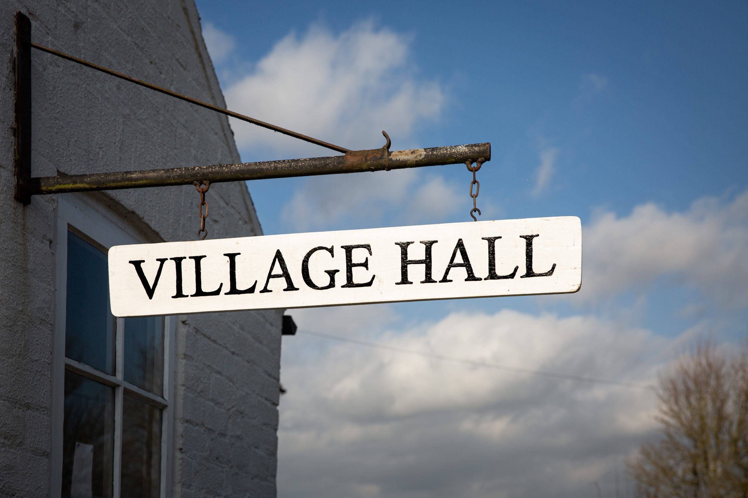 A,Village,Hall,Sign,Hanging,From,A,Local,Community,Building